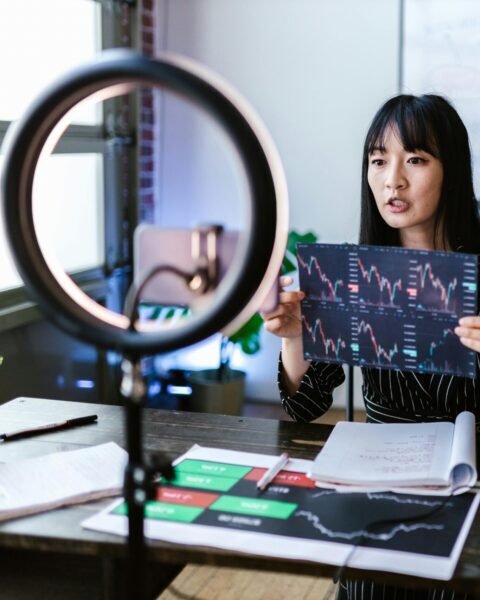 A woman vlogger discusses stock market trends using charts in a home studio.